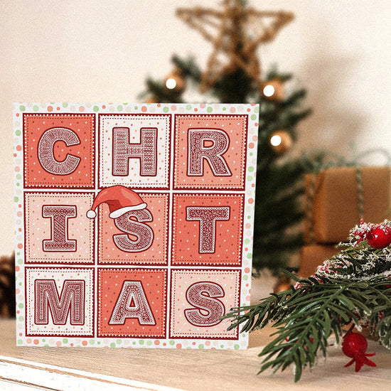Christmas-themed card with decorative text in front of a Christmas tree.